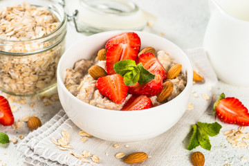 Oatmeal porridge with fresh strawberry and nuts on white background.