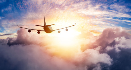 Aerial View of Commercial Airliner Jet Plane Flying in above the clouds during a colorful sunset or...