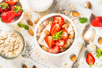 Oatmeal porridge with fresh strawberry and nuts on white background.
