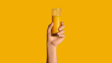 Close up of male hand showing glass with orange juice on color background, panorama