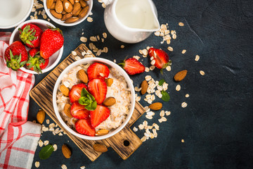 Oatmeal porridge with fresh strawberry and nuts on dark background.