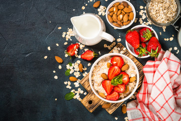 Oatmeal porridge with fresh strawberry and nuts on dark background.
