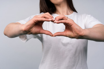 Young beautiful woman shows hands a heart shape, brunette in a white T-shirt on a white background