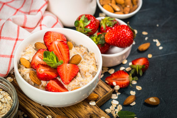 Oatmeal porridge with fresh strawberry and nuts on dark background.