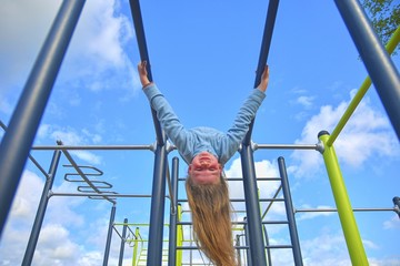 Fototapeta premium Little girl hanging upside down on parallel bars at playground.