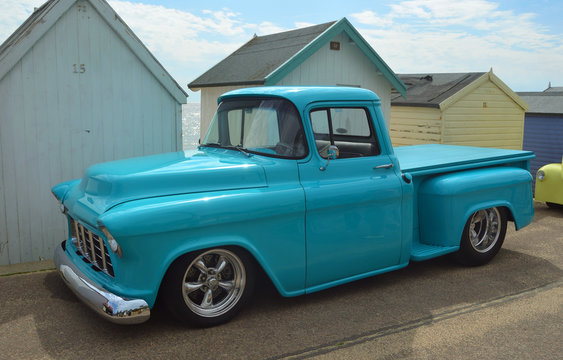  Classic Light Blue American Pick Up Truck parked in front of beach huts on seafront promenade.