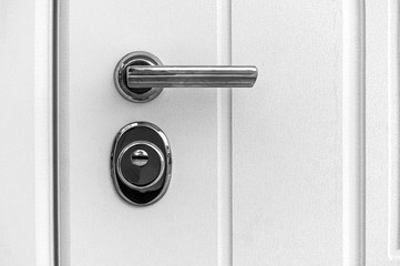 detail of a closed door with a lock handle and a white background. Metal handle and lock on the...