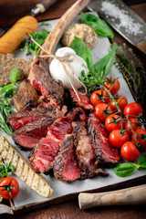 Tomahawk grilled steak cut into pieces with vegetables on a wooden Board, cooking meat barbecue
