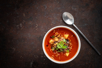 Italian tomato cream soup with meat, potatoes and green leaves in a white bowl on a rusty steel background