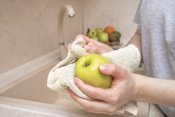 Women's hands wipe apple with a towel, against the background of a fruit basket. Hygiene. Stay home. Quarantine. Pandemic Coronavirus.