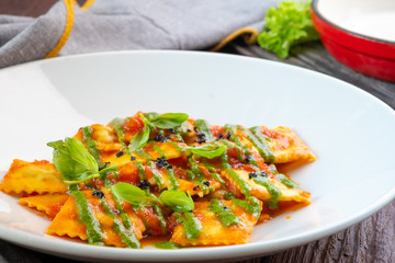 Classic ravioli with tomato sauce and Basil leaves on a white plate, close up