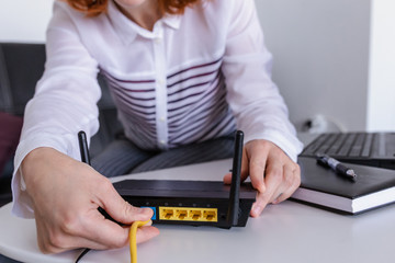 Redhead woman connects the internet cable to the router's socket. Fast and wireless internet concept