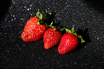 3 strawberries on a black background. On the brilliant dark background of the three berries. Fresh fruit.