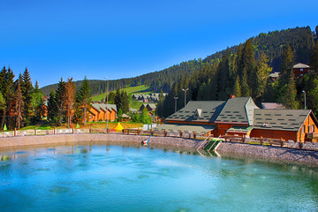 Beautiful view of the summer slope with forest, lake and wooden houses in resort Bukovel, Ukraine. Bukovel is the largest ski resort in Eastern Europe situated in Ukraine