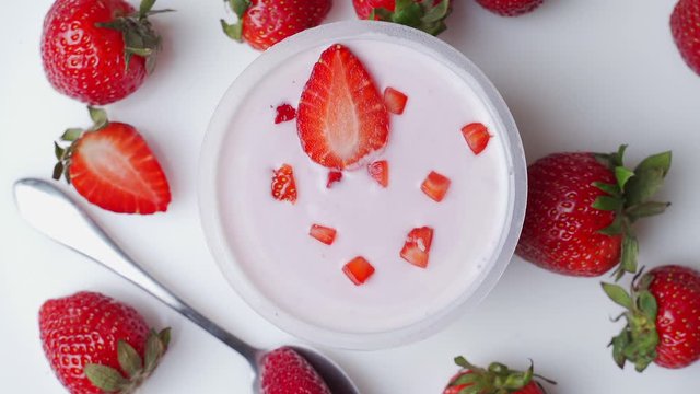 Bowl of delicious yogurt and strawberries rotates on the table. The view from the top