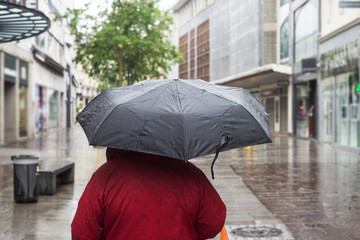 Portrait of woman walking in the street wearing a red coat and a black umbrella