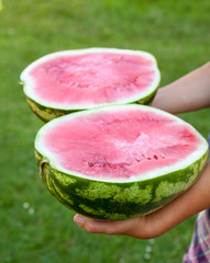 Hands holding a watermelon cut into halves.