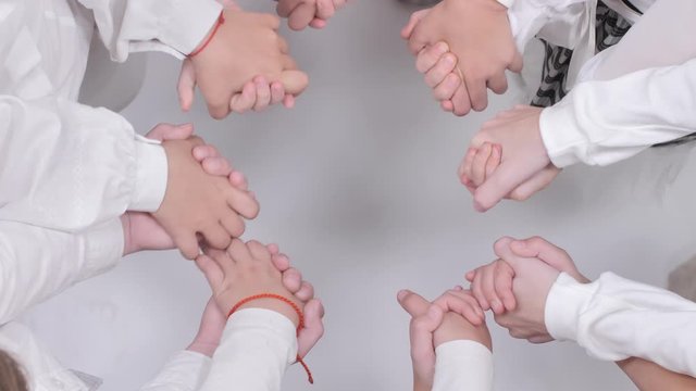 Children hold fists in a circle and hold hands on a white background.