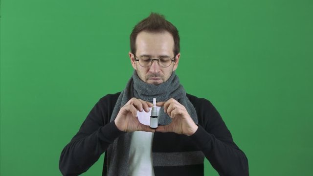 The man is sick, runny nose. Takes medicine in nose spray. A scarf around the neck. Respiratory disease, virus. On a green background, chromakey