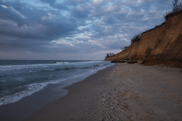 Dramatic sea coast with mood low clouds and waves. Black sea beach with high mud coast, Odessa, Ukraine