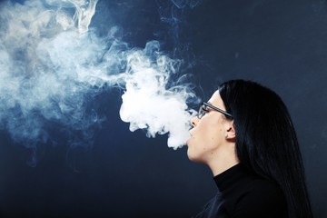 Attractive european girl with black hair and glasses posing in studio and smoking a cigar on isolated background. Style, trends, smoking, fashion concept.