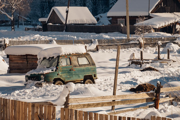 Russian village: old soviet off-road car parked at the snowy courtyard with wooden houses and manure