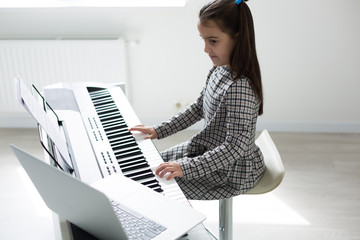 Little girl distance learning the piano online during quarantine. Coronavirus concept.