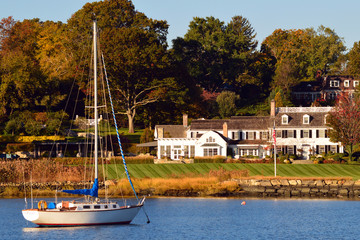 A rich life: A sailboat is moored at a luxury waterfront homes in Greenwich Connecticut, often considered one of the wealthiest towns in America - obrazy, fototapety, plakaty