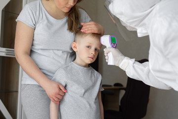 Pediatrician or doctor checks elementary age boy's body temperature using infrared forehead thermometer gun for virus symptom - epidemic coronavirus outbreak concept