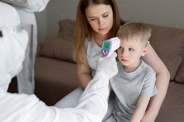 Coronavirus. Doctor checks boy's body temperature using infrared forehead thermometer gun for virus...