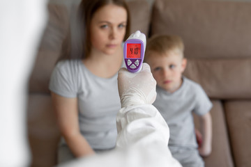 Doctor checks the body temperature of the girl and her son using an infrared thermometer gun on the...