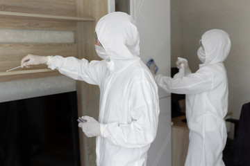 Virologists, people in protective suits carry out the disinfection in the apartment. Wipe furniture...