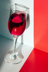 Glass glass of red wine on a red-and-white background with highlights from sunlight. The concept of the alcoholic tastings