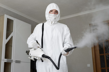 .Disinfector in a protective suit conducts disinfection in home. professional disinfection against...