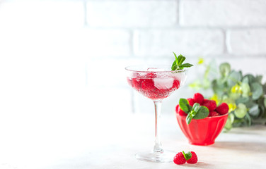 Raspberry lemonade with mint and ice in a glass on a light concrete background.