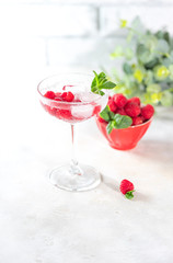 Raspberry lemonade with mint and ice in a glass on a light concrete background.