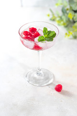 Raspberry lemonade with mint and ice in a glass on a light concrete background.