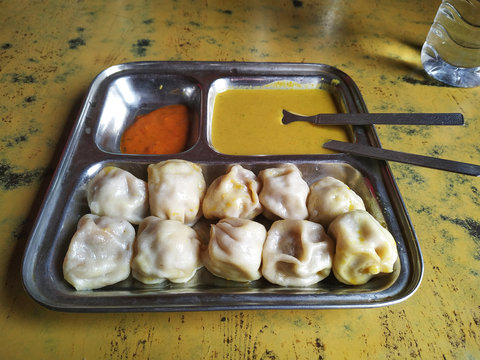 View of steamed spicy momo stuffed with domestic water buffalo meat with two sauces served on a metallic dish in home restaurant in Ramechhap village, Nepal.