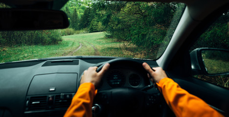 Driver dressed bright orange jacket driving a modern off road right hand drive RHD car on the mountain green forest country road. POV inside car windscreen view point. Safely auto driving concept.