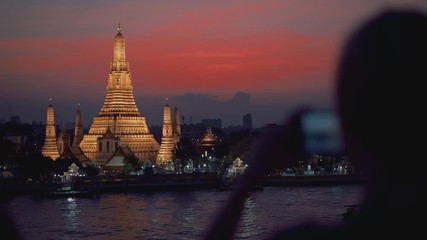 Right to left pan real time establishing shot of Wat Arun, a Buddhist temple in Bangkok, Thailand. Wat Arun Temple at sunset. Tourist takes photos of the temple, January 12, 2020 in Bangkok, Thailand.