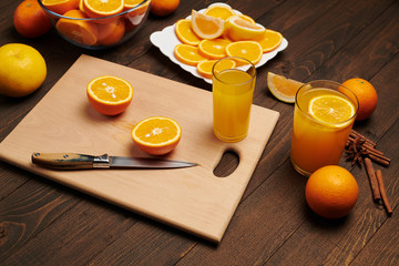 Fresh orange fruit whole and sliced on a wooden table, cutting board and kitchen knife. A plate full of citrus slices - natural and healthy food. Glass of fruit cocktail.