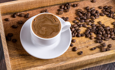 A Cup of coffee milk and nearby coffee beans in a wooden box on a dark wooden background.