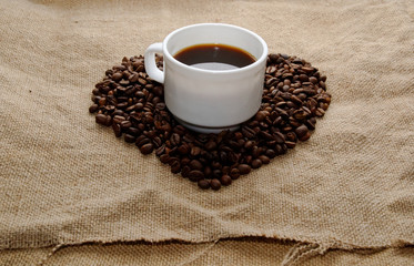 heart made from coffee beans top in the center a white cup with coffee.