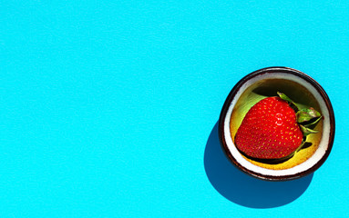 Fresh, ripe strawberries in a cup on a blue paper background, top view with copy space. Delicious berry dessert