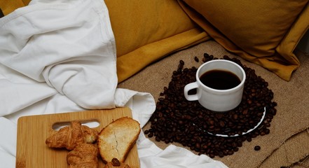 coffee beans sprinkled on a white saucer from above a cup with coffee on burlap.