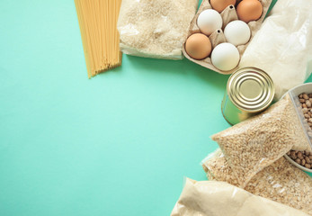 pearl barley, rice, stew, can, canned food, sugar, paper bag, eggs, spaghetti, oatmeal lie on a mint-colored background, food delivery concept