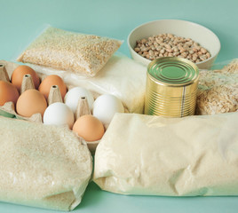 pearl barley, rice, stew, can, canned food, sugar, paper bag, eggs, spaghetti, oatmeal lie on a mint-colored background, food delivery concept