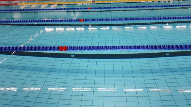 Panning video over empty swimming pool for training with crystal clear water and blue yellow lanes, small ripples on pool surface, reflection from lights