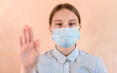 Teenager girl 12-15 years old, in a medical mask covers her face, stop hand gesture, attention is dangerous, COVID-19 sars-cov-2 epidemic pandemic virus outbreak protection concept.