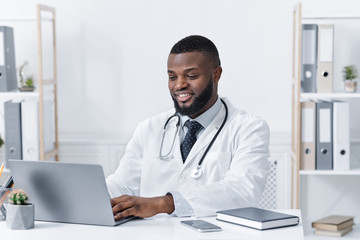 Cheerful black doctor working at his workplace